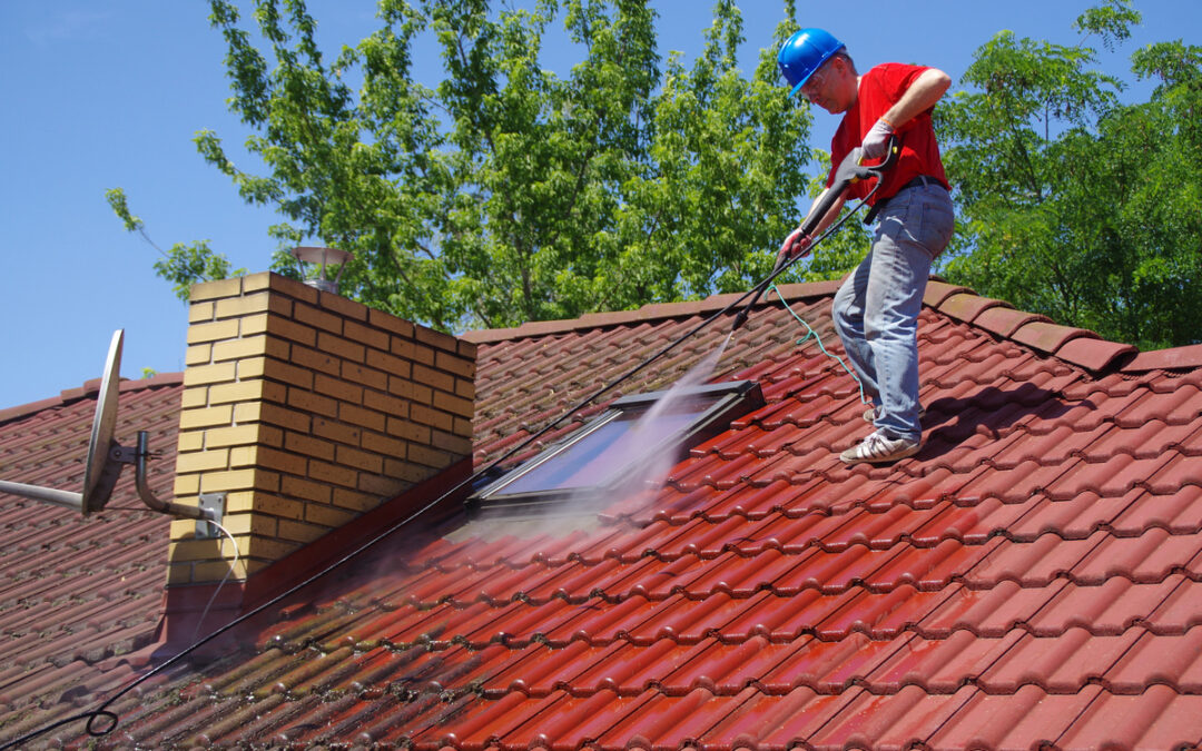 House roof cleaning with pressure tool. Worker on top of building washing tile with professional equipment.