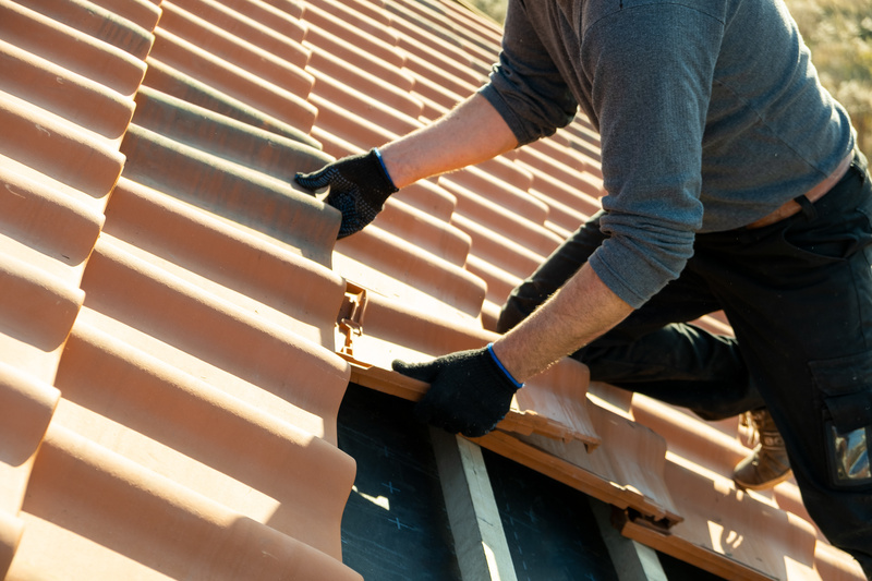 Closeup of worker hands installing yellow ceramic roofing tiles covering residential building roof undergoing roof replacement.